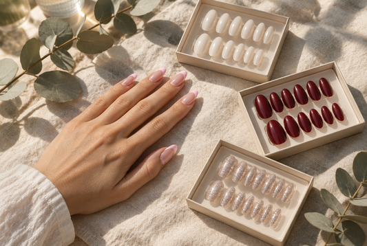 Hand with blush pink French tip press-on nails beside three open press-on nail sets